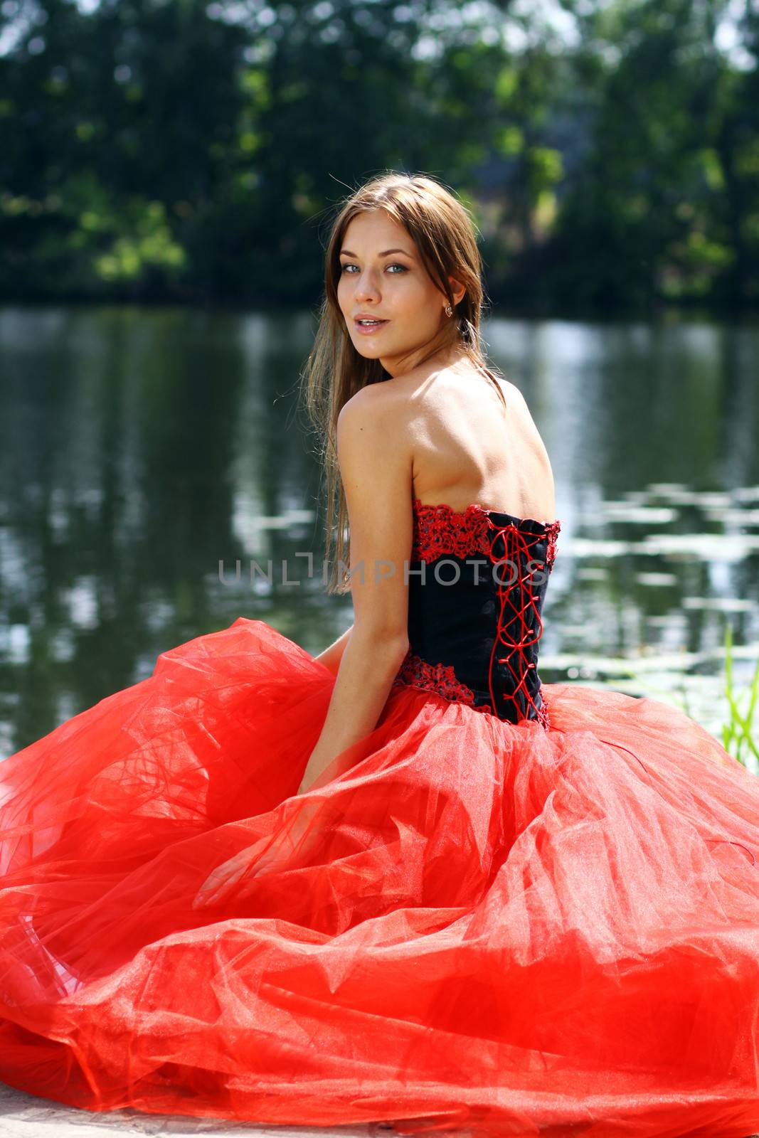 Smiling woman in a red dress sitting near river
