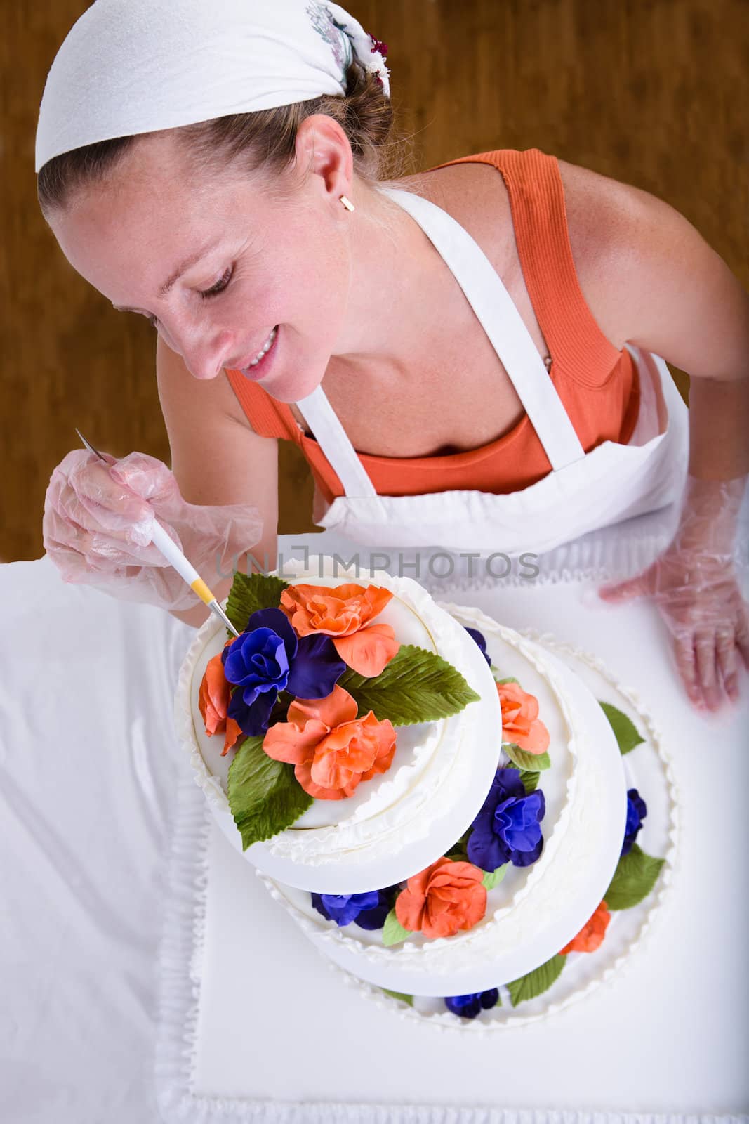 Woman with white bandanna giving to a wedding cake latest small retouches with love, shot from above