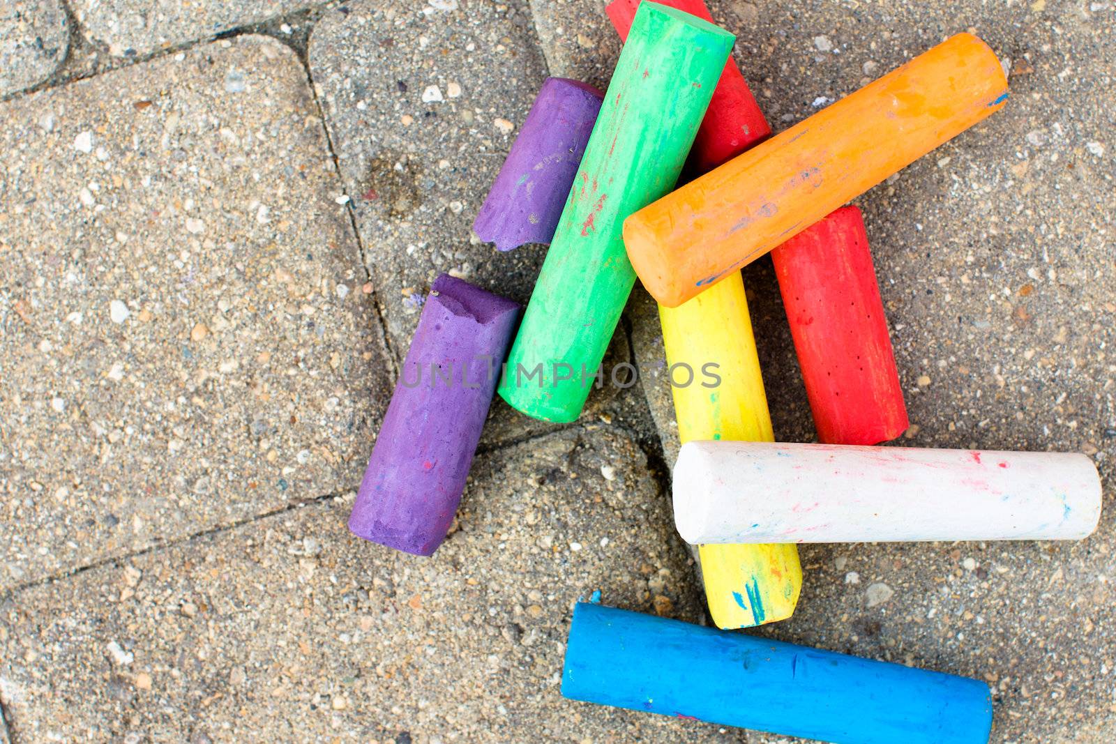 Colorful chalks naturally on the paver street some of them broken some of them not. They have purple, green, orange, yellow, red,white and blue colors