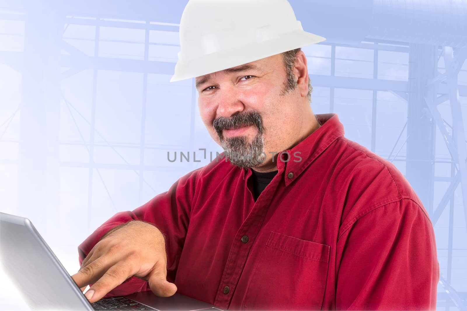 Hardhat technician smiling at camera trustfully while working on the laptop