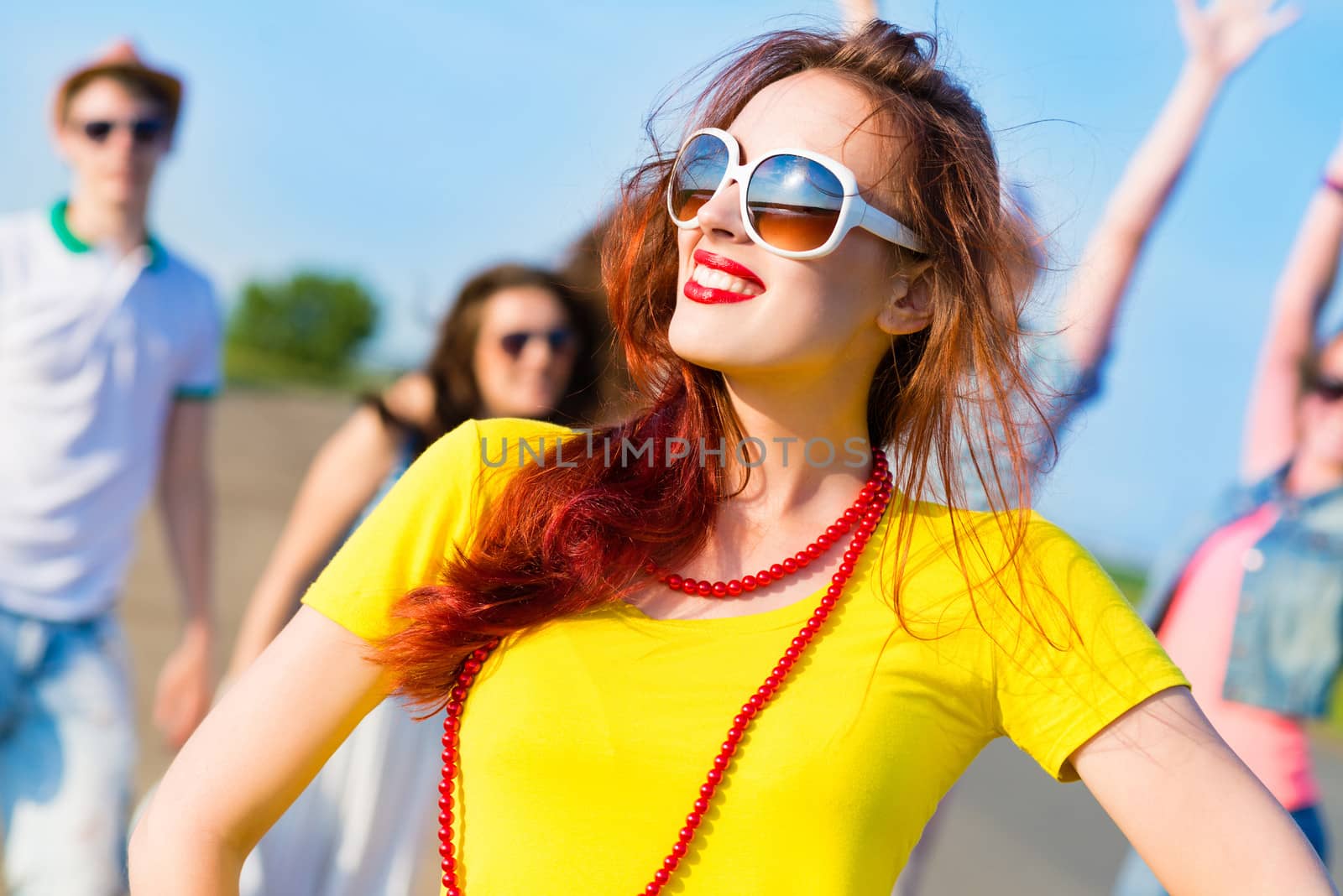 stylish young woman in sunglasses on the background of blue sky and friends