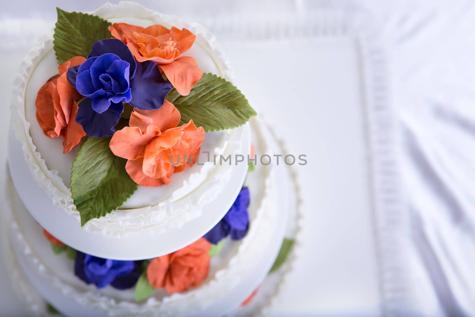 Three tier fondant  ruffled white wedding cake decorated with orange and purple gum paste roses and green leafs, shot from above