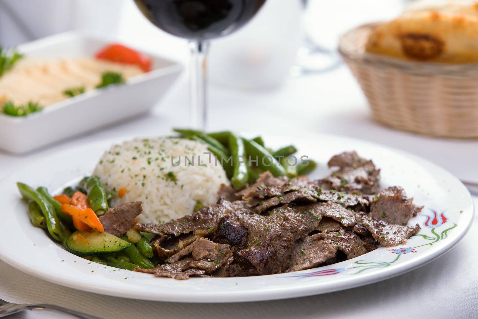 Gyro Doner garnished with rice Pilaf and vegetables partnered with hummus, pita bread and red wine