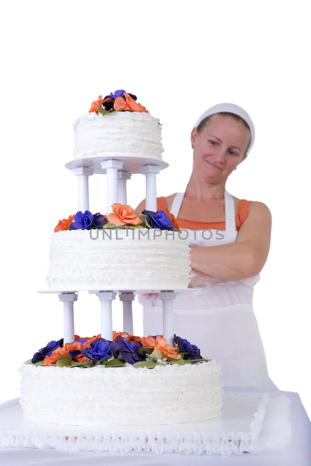 Baker lady giving to a wedding cake latest proud look in her apron and white bandanna, cake has fondant ruffles on the side and decorated with orange and purple gum paste roses
