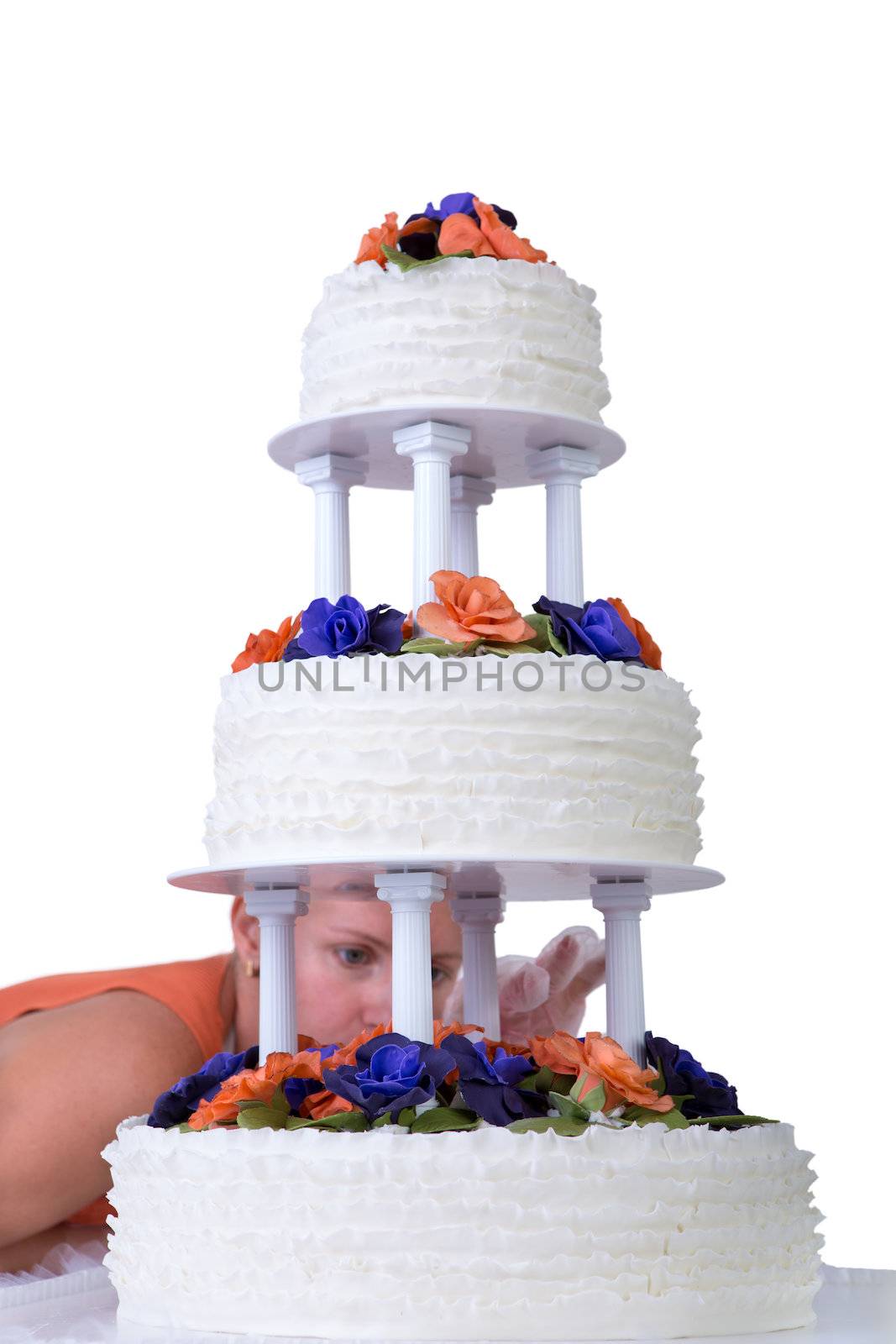 Baker lady giving to a wedding cake latest small retouches, cake has fondant ruffles on the side and decorated with orange and purple gum paste roses