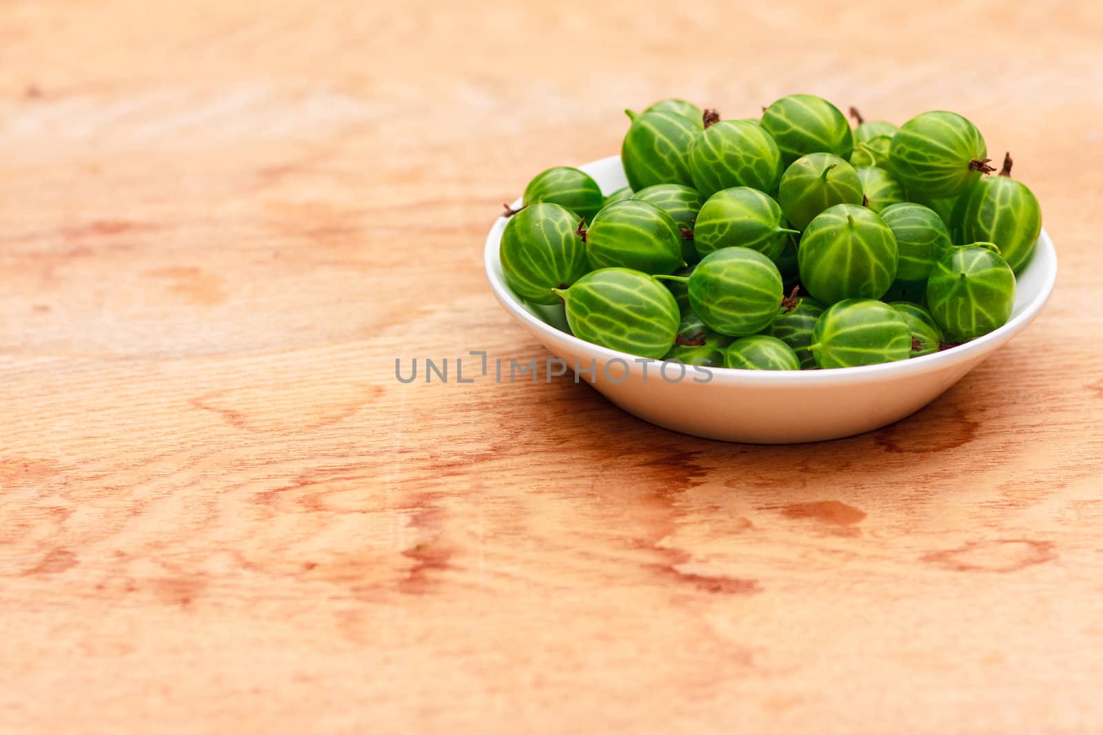 White Dish Filled With Succulent Juicy Fresh Ripe Green Gooseberries On An Old Wooden Table Top.