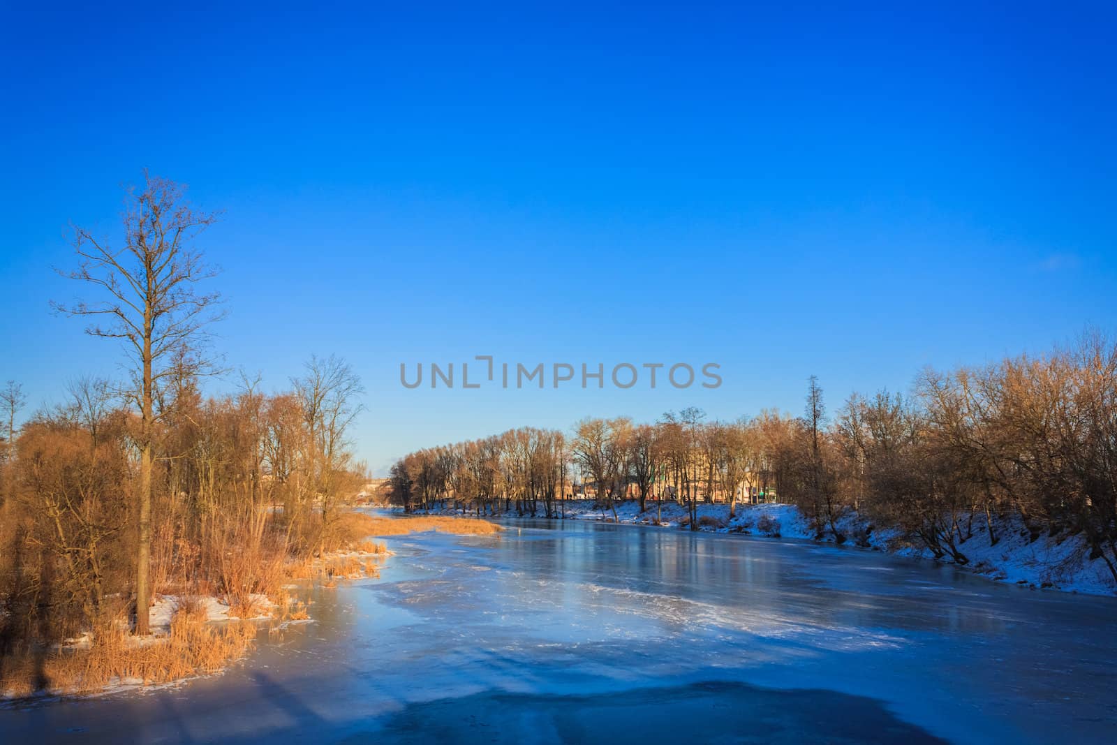 Winter River With Ice On A Surface And Snowy Coast Under Blue Clear Sky