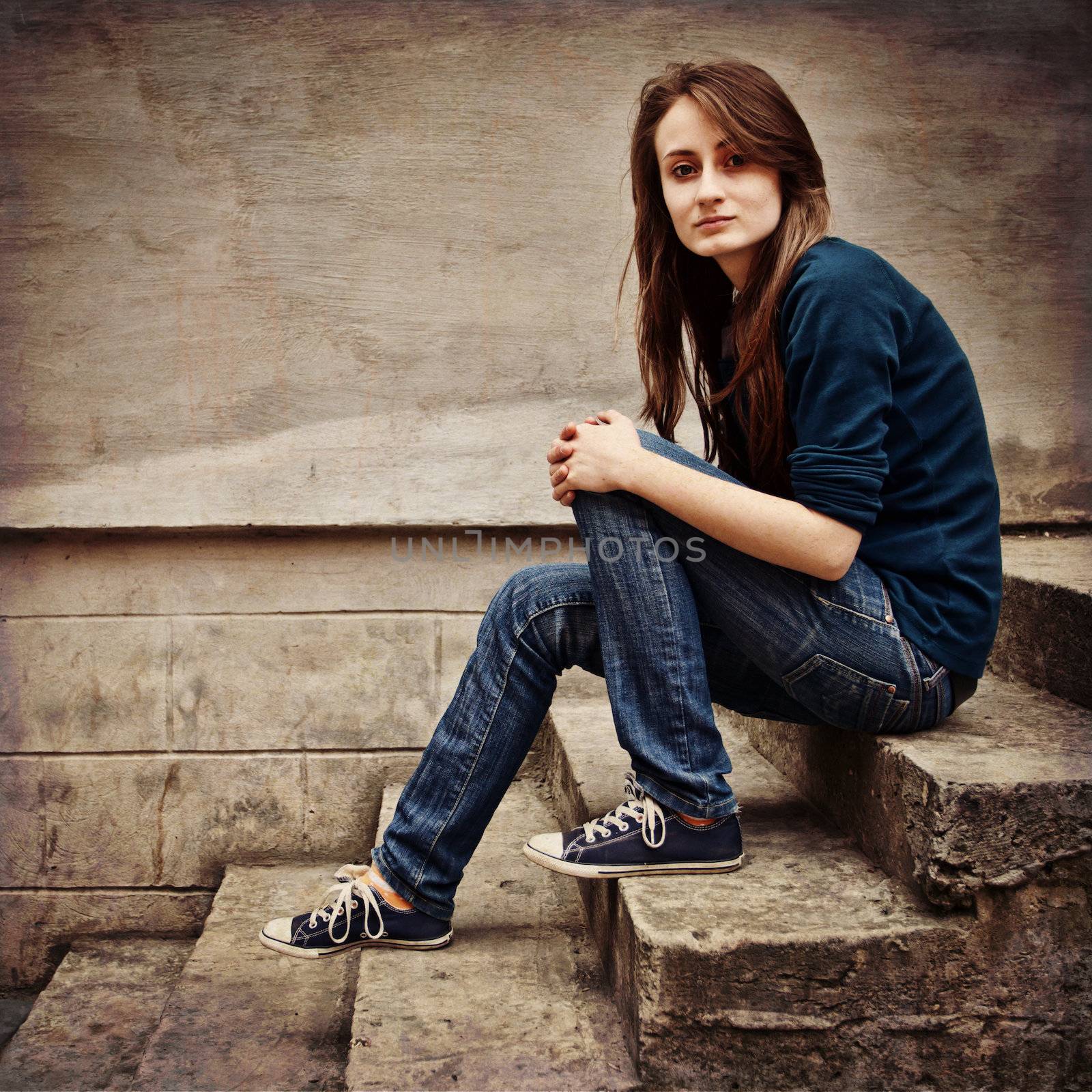Teen girl sitting on stairs against grungy wall. square photo with grunge texture.