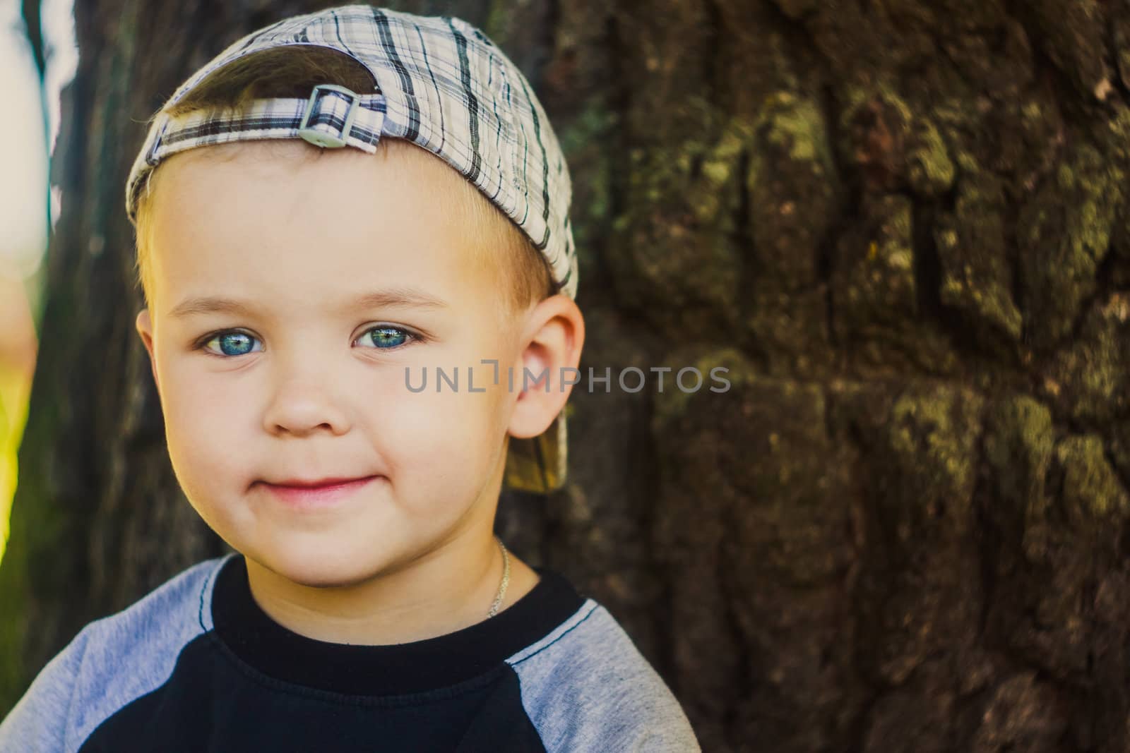 Happy caucasian child boy smiling outdoors with stripped cap, green nature background
