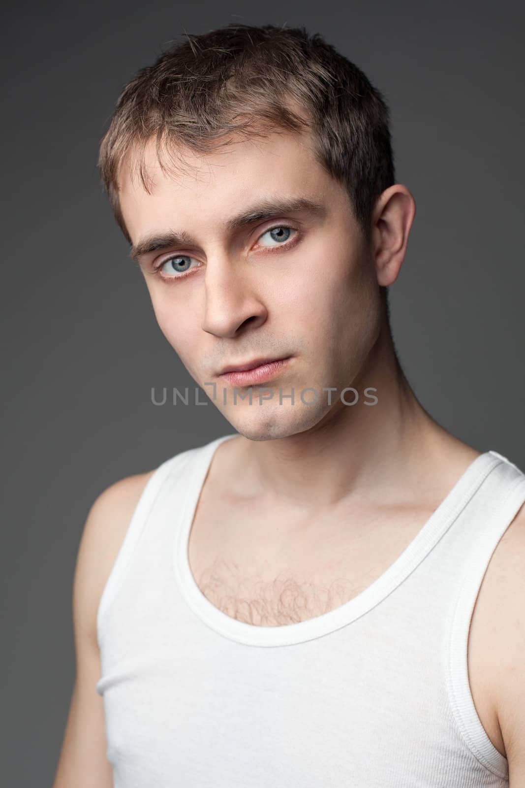 Portrait of the young beautiful man in white t-shirt posing over gray backgroun