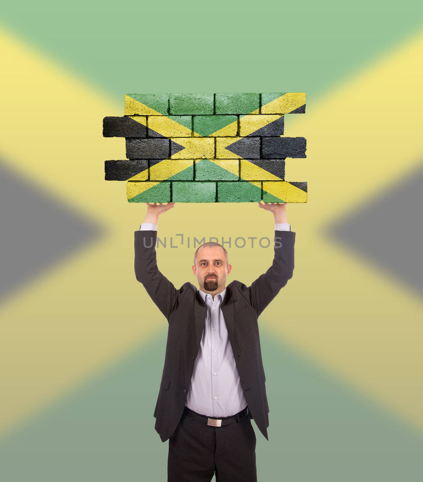 Businessman holding a large piece of a brick wall, flag of Jamaica, isolated on national flag