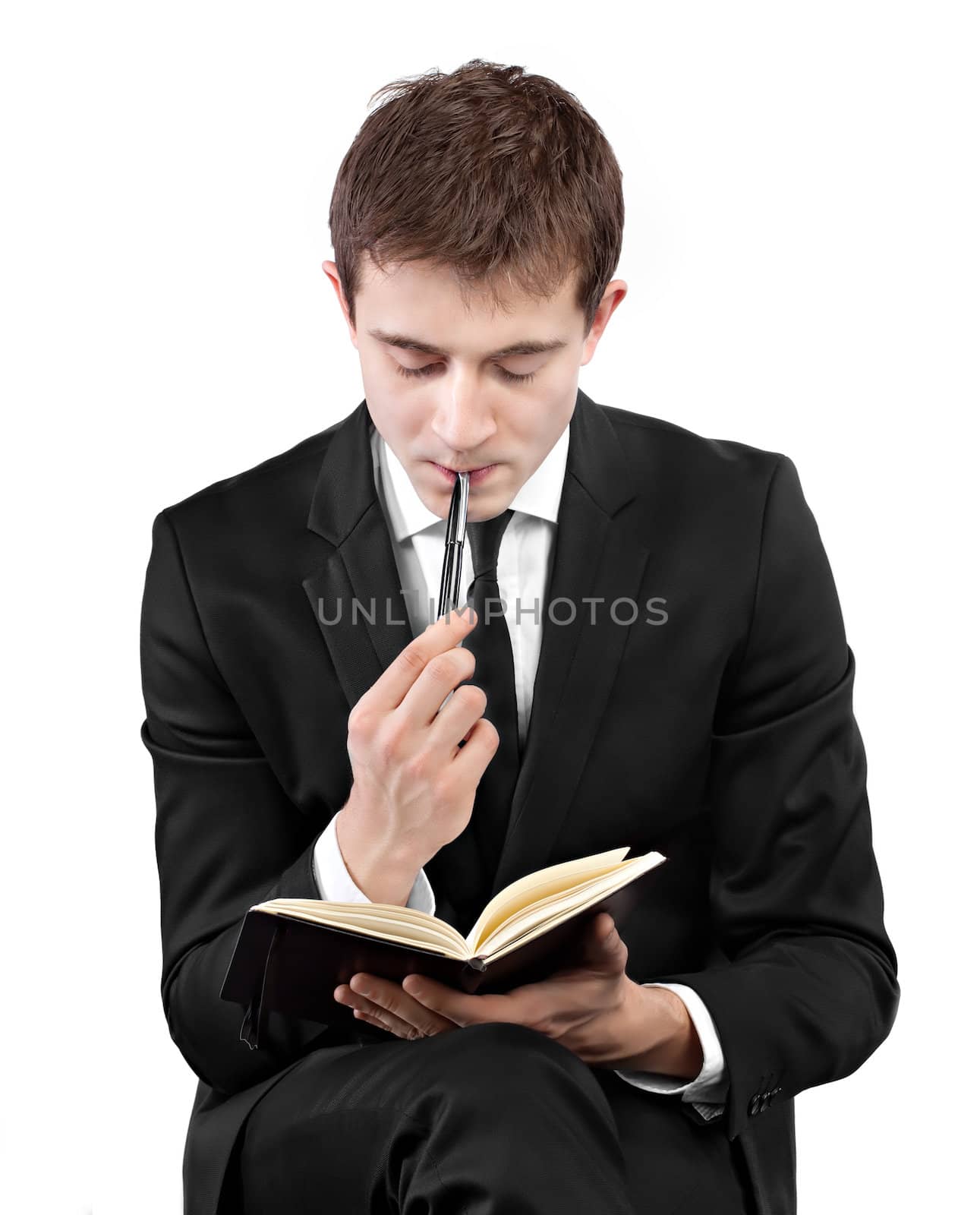 Handsome young businessman in black suit thinking with pen and whatching into notebook