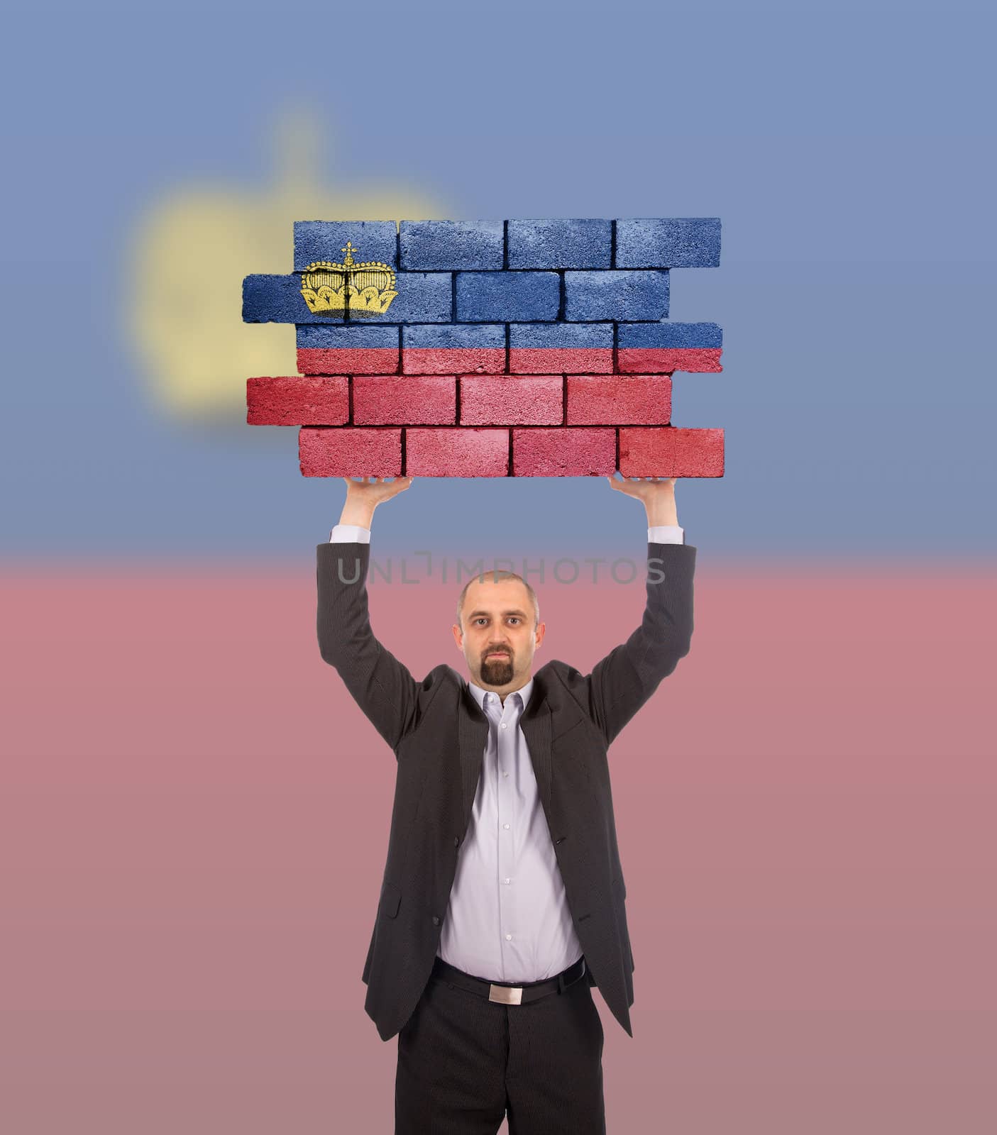 Businessman holding a large piece of a brick wall, flag of Liechtenstein, isolated on national flag