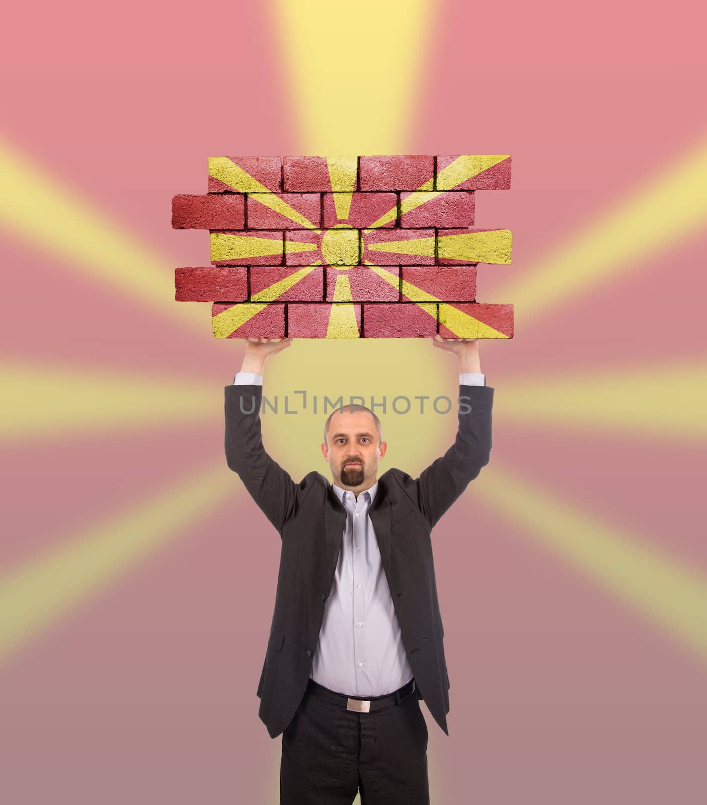 Businessman holding a large piece of a brick wall, flag of Macedonia, isolated on national flag