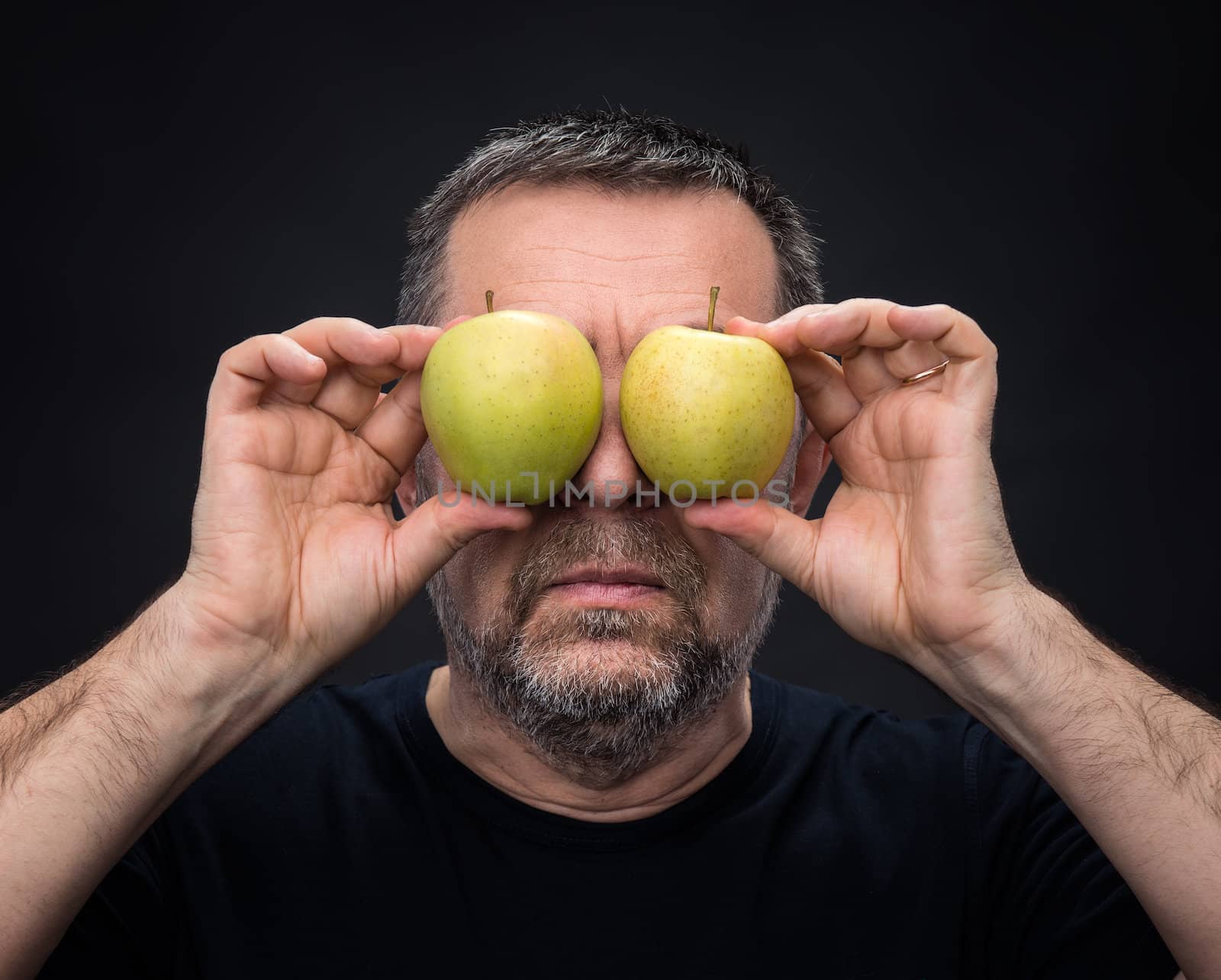Middle-aged man in black with two green apples instead of eyes