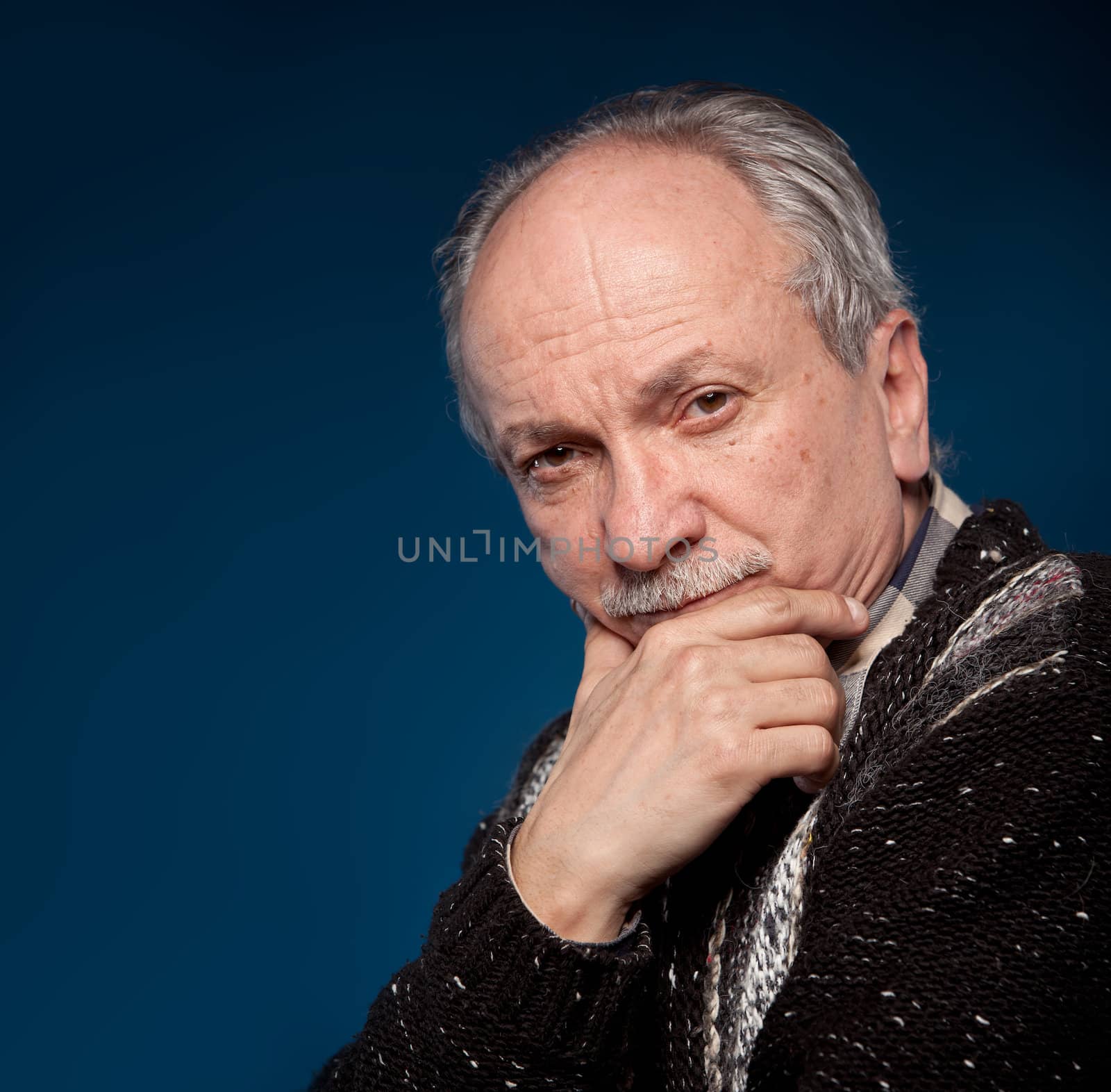 Portrait of an elderly man with a serious expression on a dark blue background with room for text.