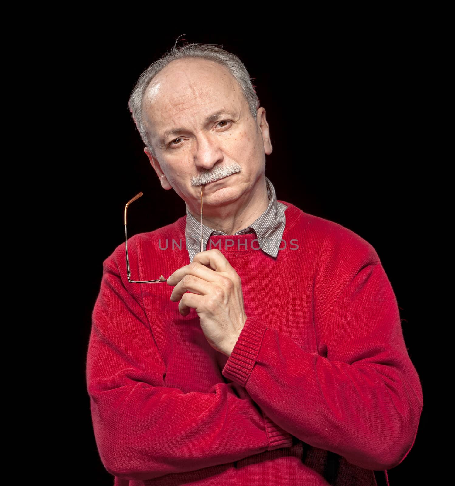 Portrait of an thoughtful  elderly man with glasses in his hands on a dark  background