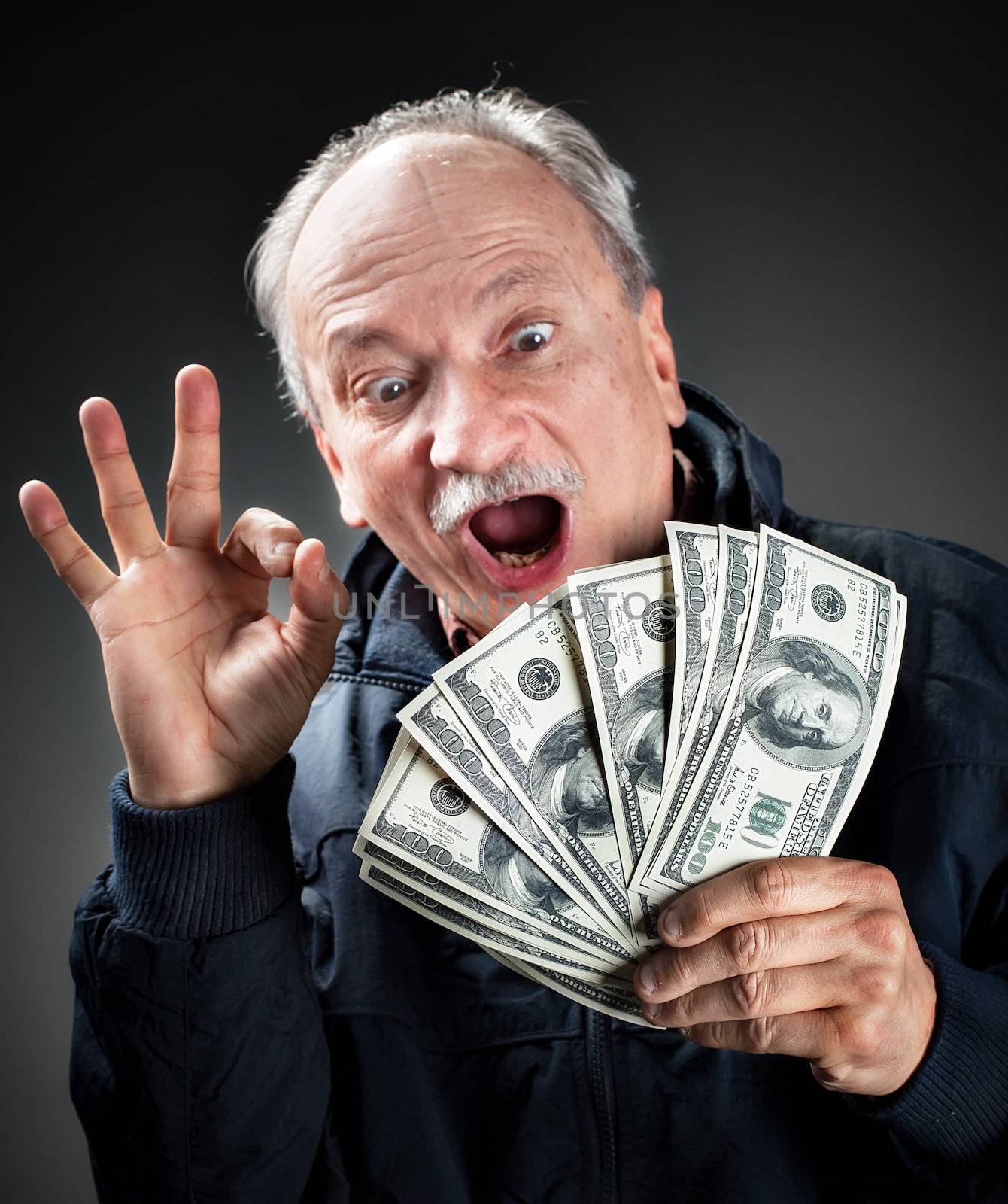Happy elderly man showing fan of money and sign OK with fingers. Focus on money.  Softly blurred face