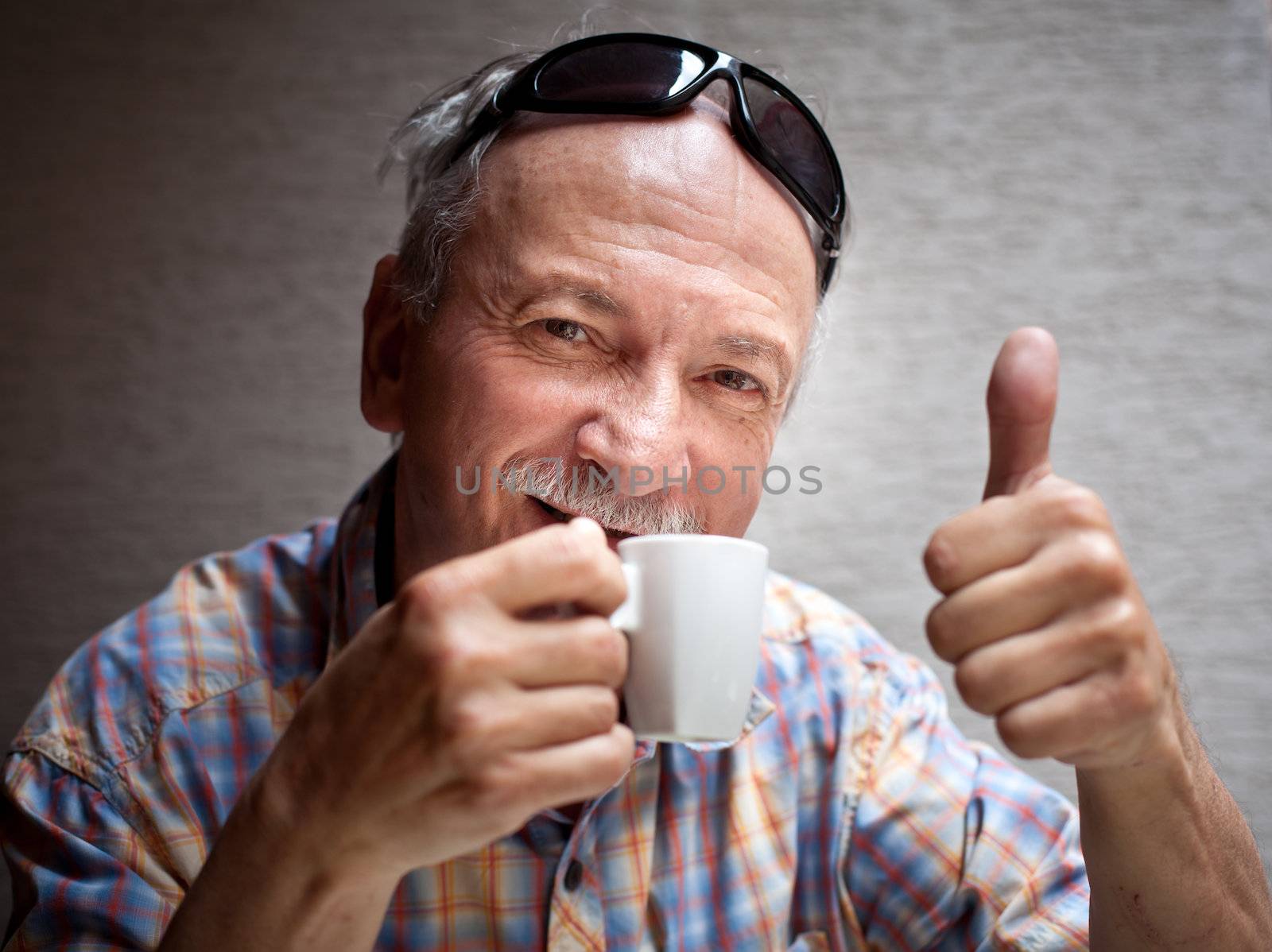 Portrait of smart old man drinking cup of coffee and showing sign OK with fingers