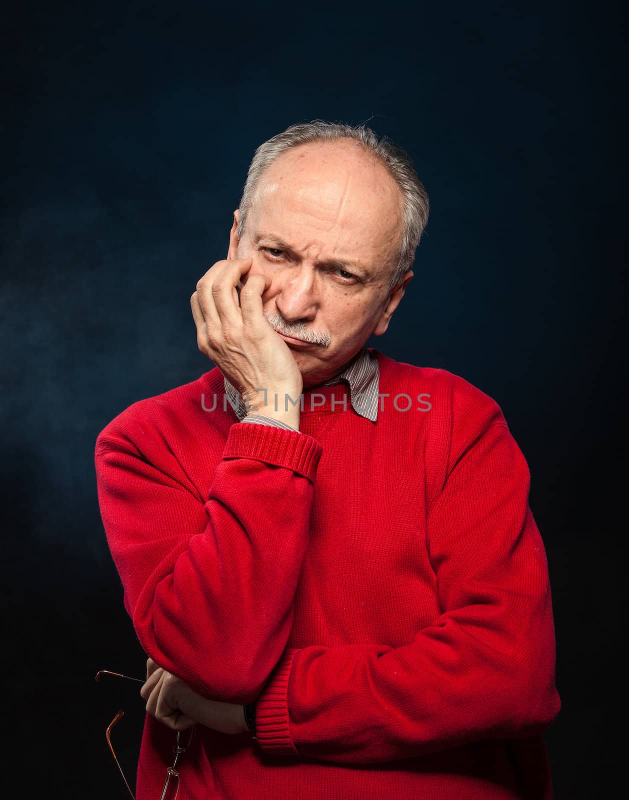 Portrait of a thoughtful elderly man with glasses in a red sweater