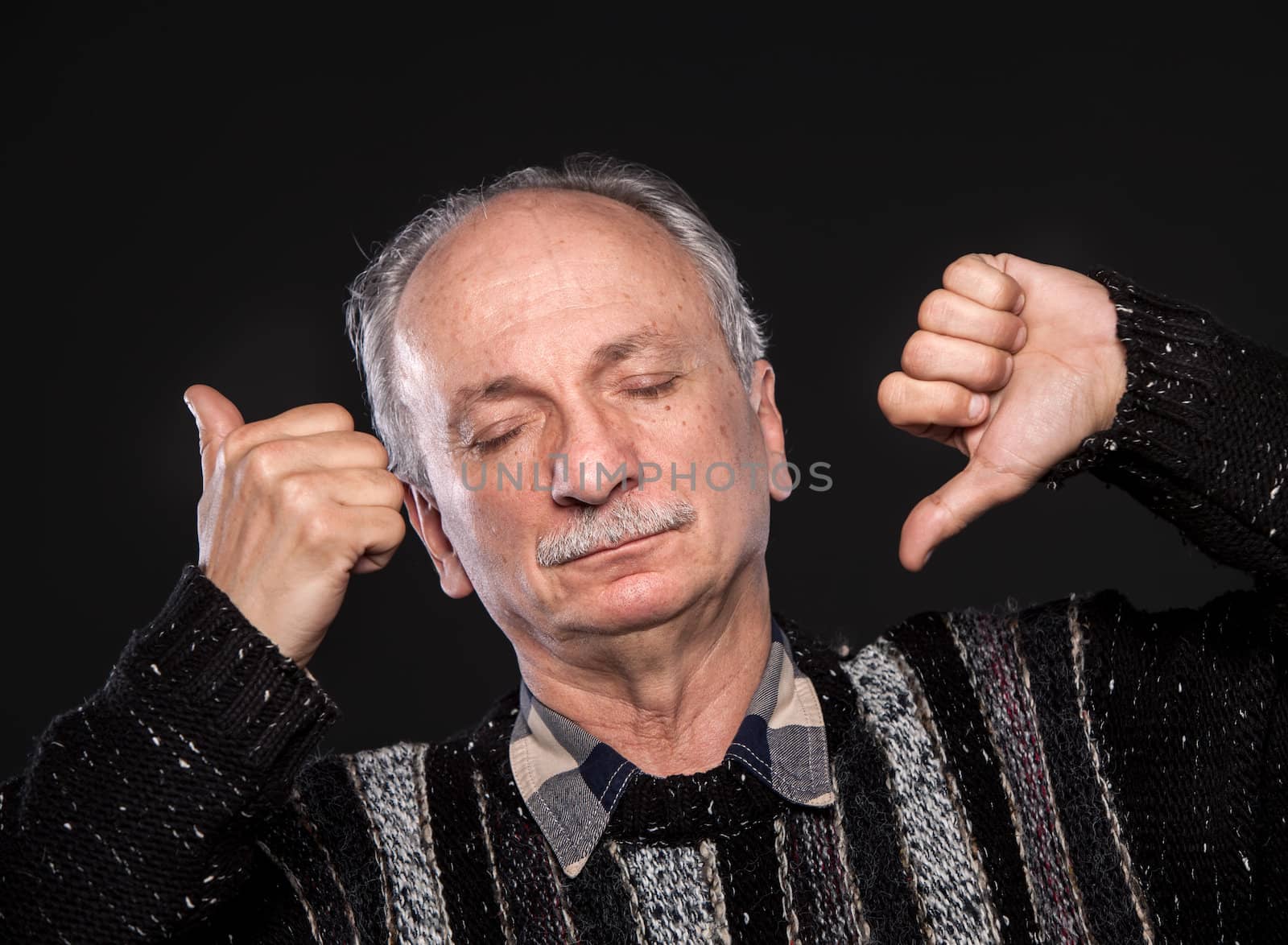 Thoughtful elderly man with closed eyes and thumb up and down