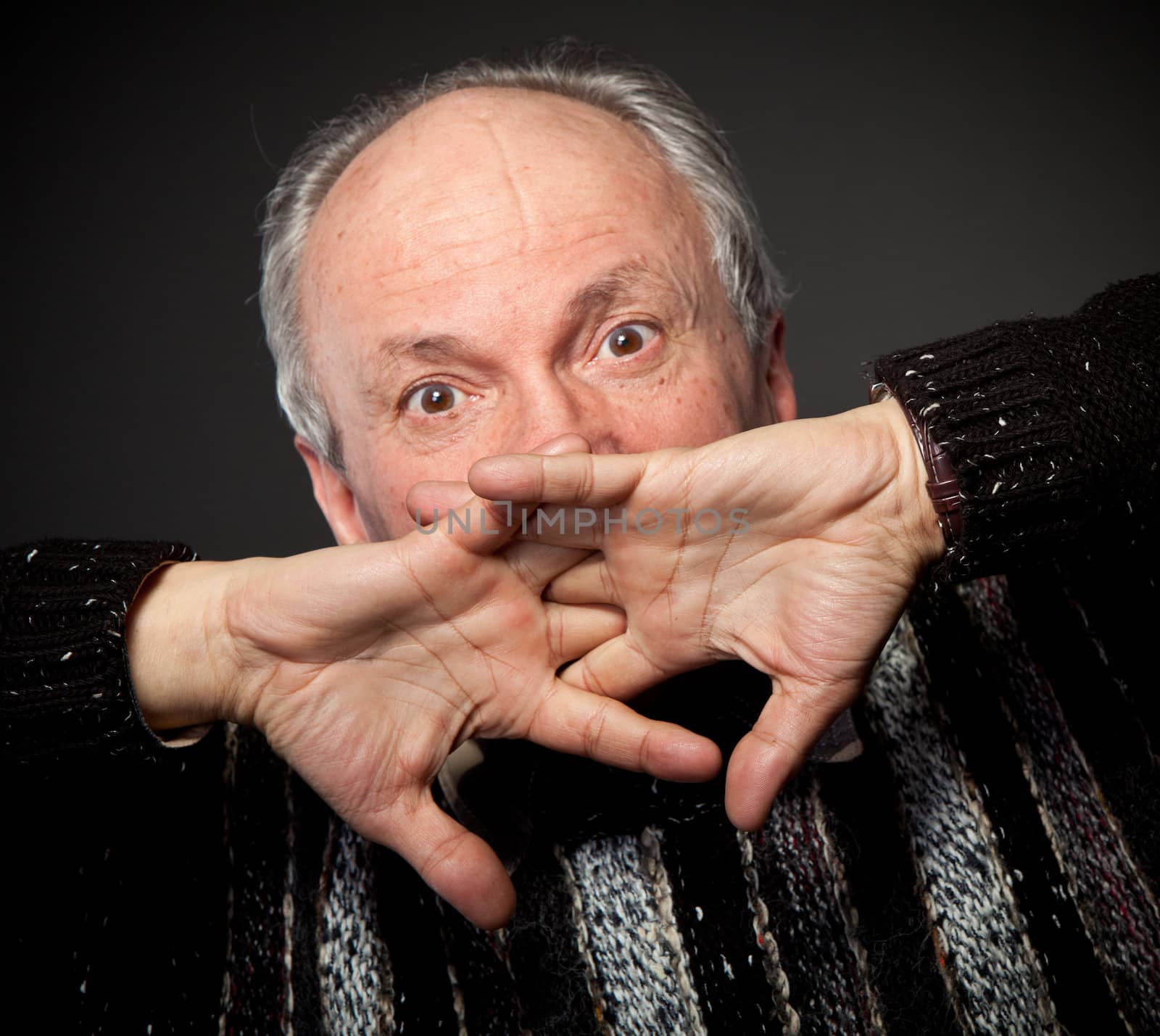 Handsome senior man with a surprised expression covers his face by hands