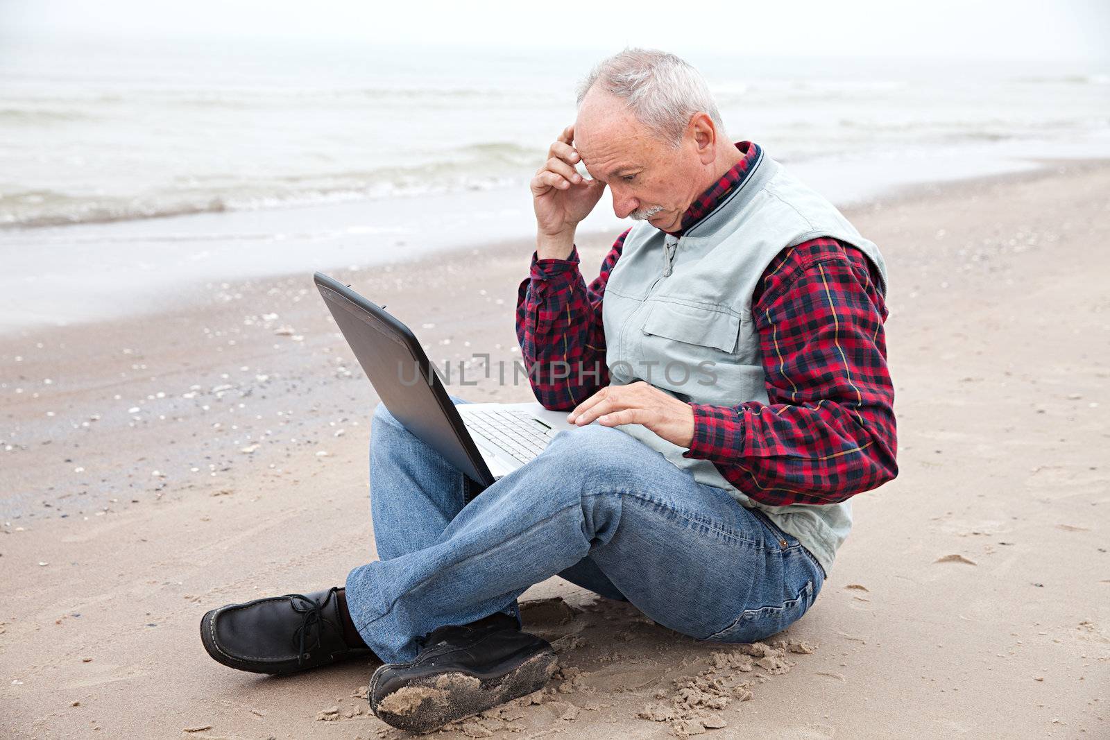 Senior businessman sitting with notebook on beach