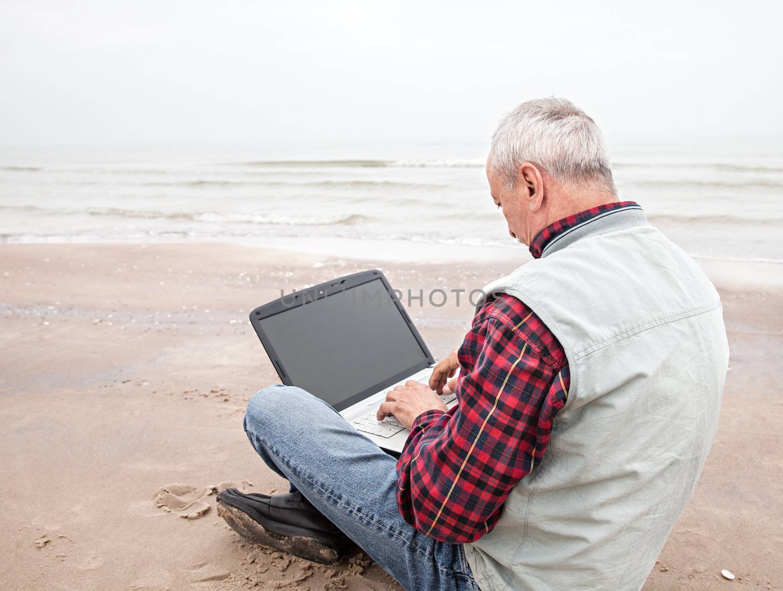 Senior businessman sitting with notebook on beach