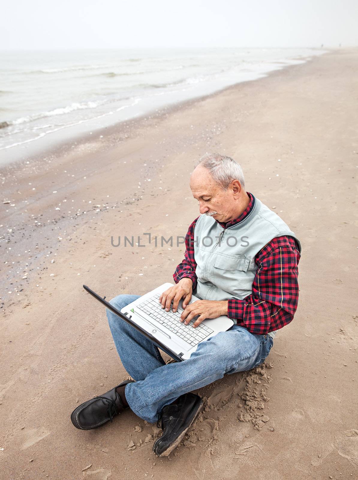 Senior businessman sitting with notebook on beach