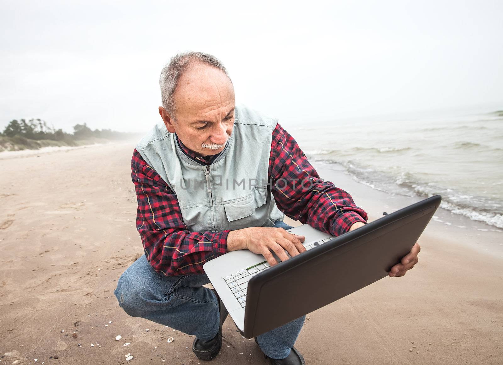 Senior businessman on beach working with notebook