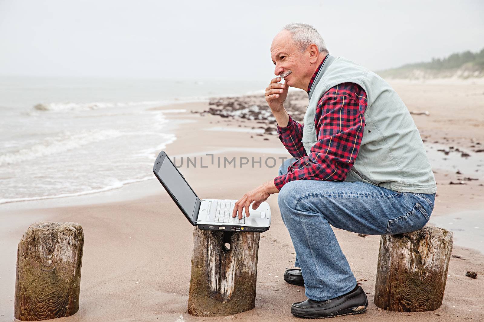 Senior businessman on beach working with notebook