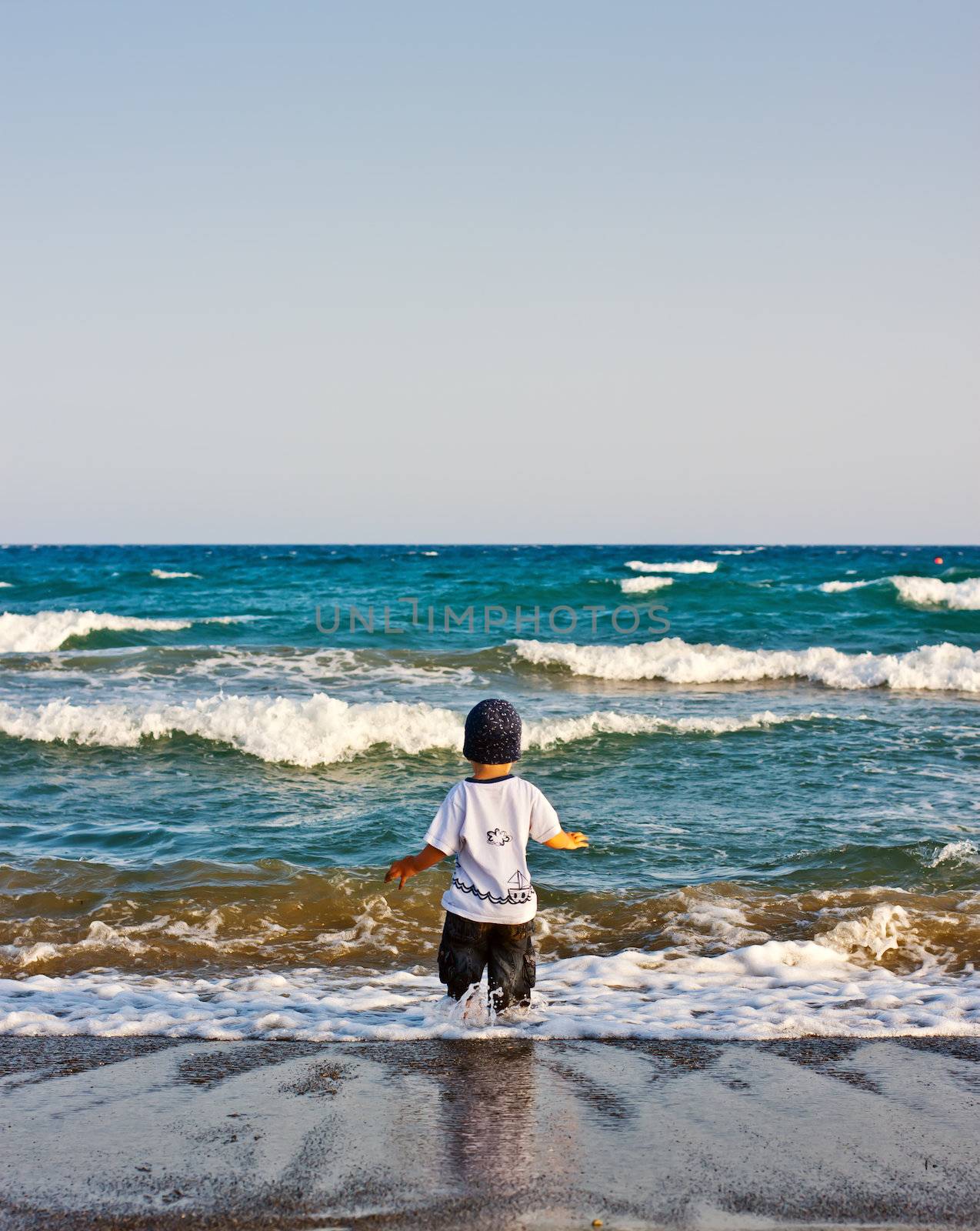 The boy stands on the beach and looks at sea