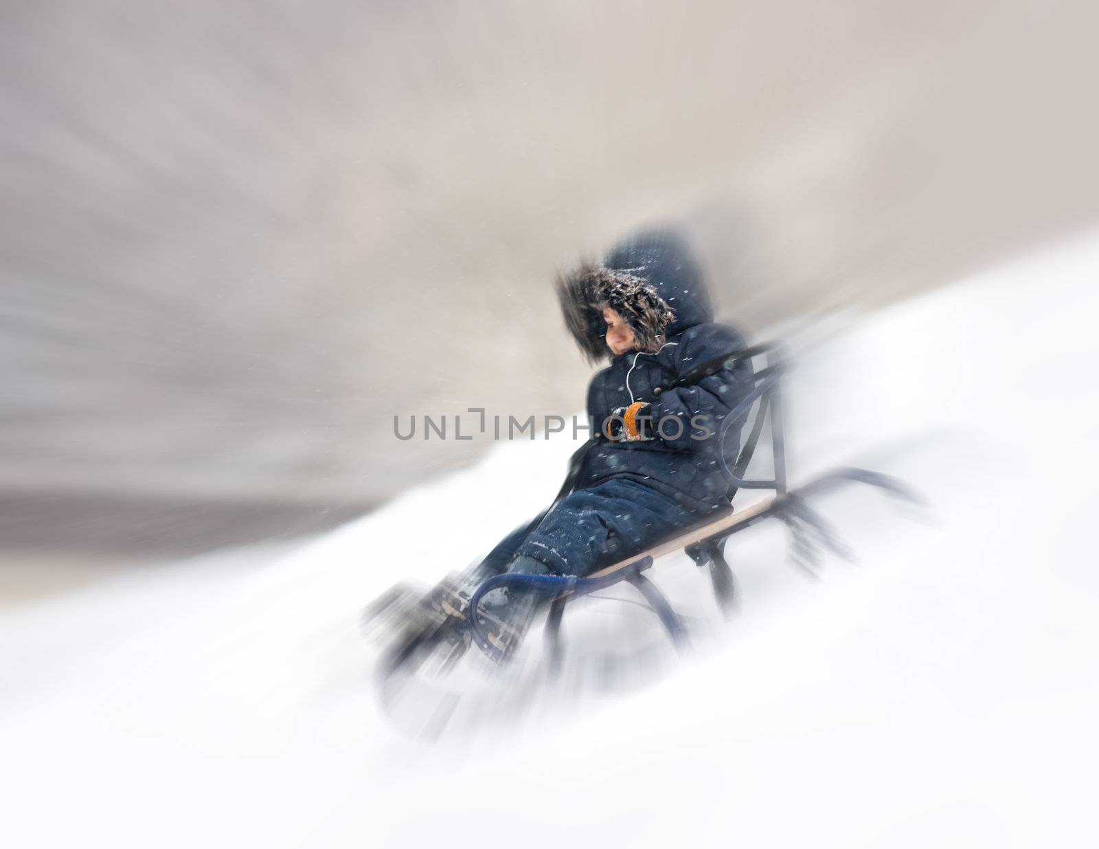 Young boy on sledge sliding fast down snowy hill with motion blur