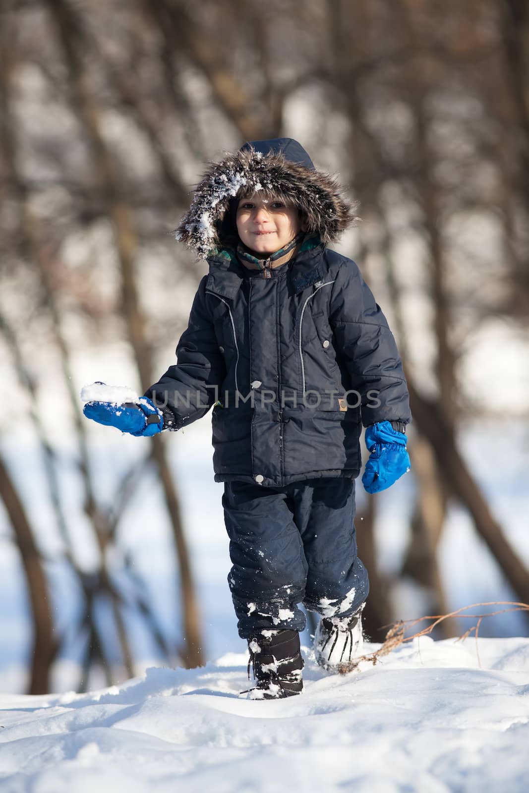 Cute boy in a winter jacket, playing with snow