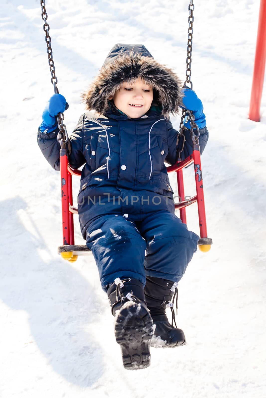 Kid swinging in the snow in sunny winter day