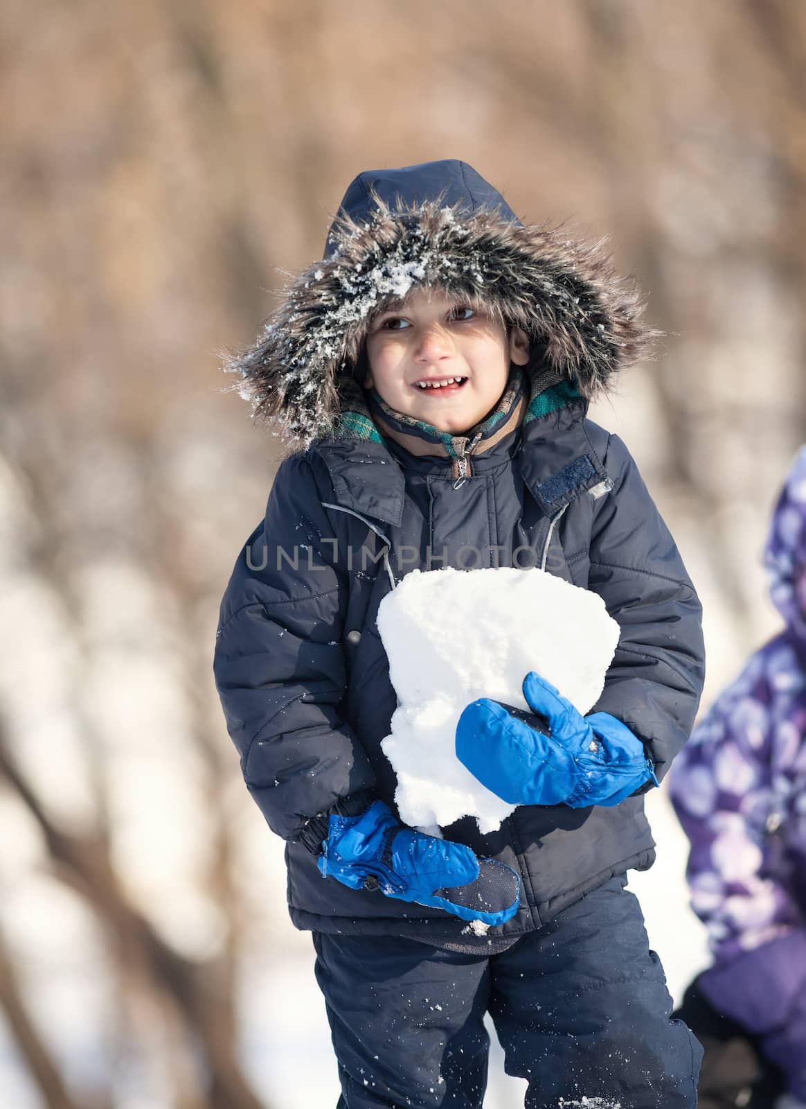 Cute boy in a winter jacket, playing with snow