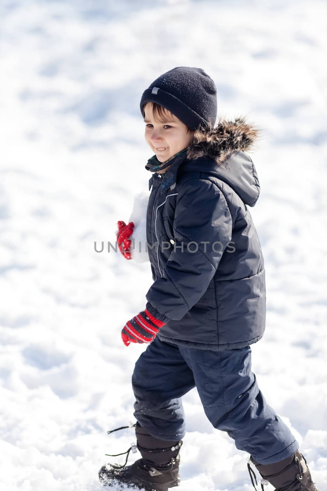 Cute boy playing with snow in the winter park in sunny day
