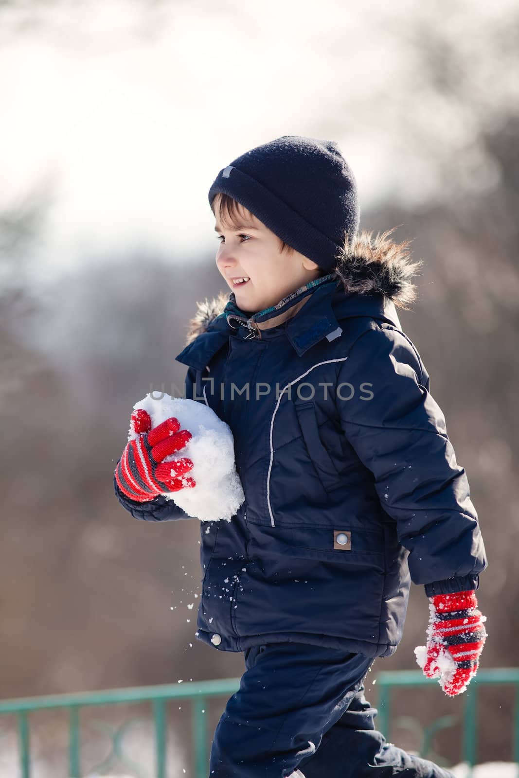 Cute boy in a winter jacket, playing with snow