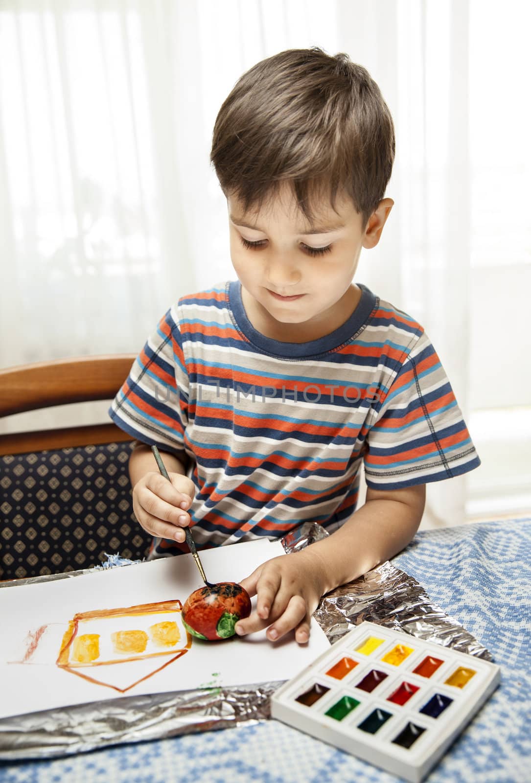 
Home and family. Little boy draws house and easter egg with watercolor