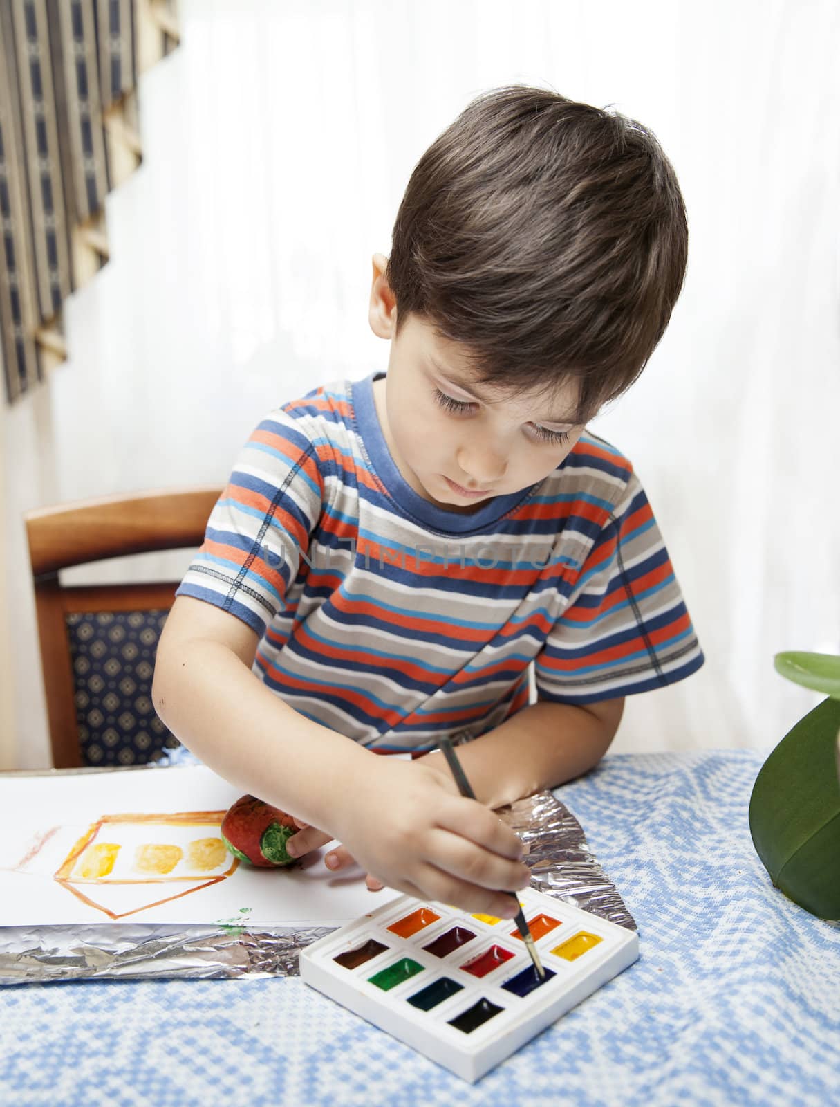 
Home and family. Little boy draws house and easter egg with watercolor