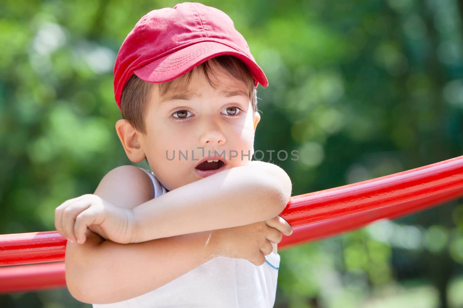 3-4 years old boy standing on a playground in a red cap on the blurred natural background