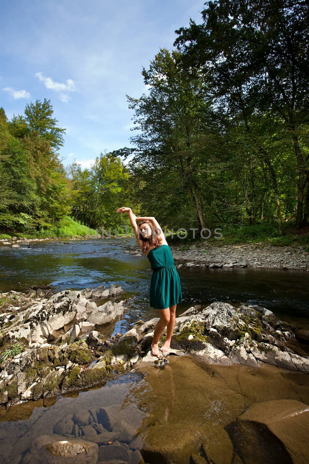 Young woman with raised hands resting near forest river