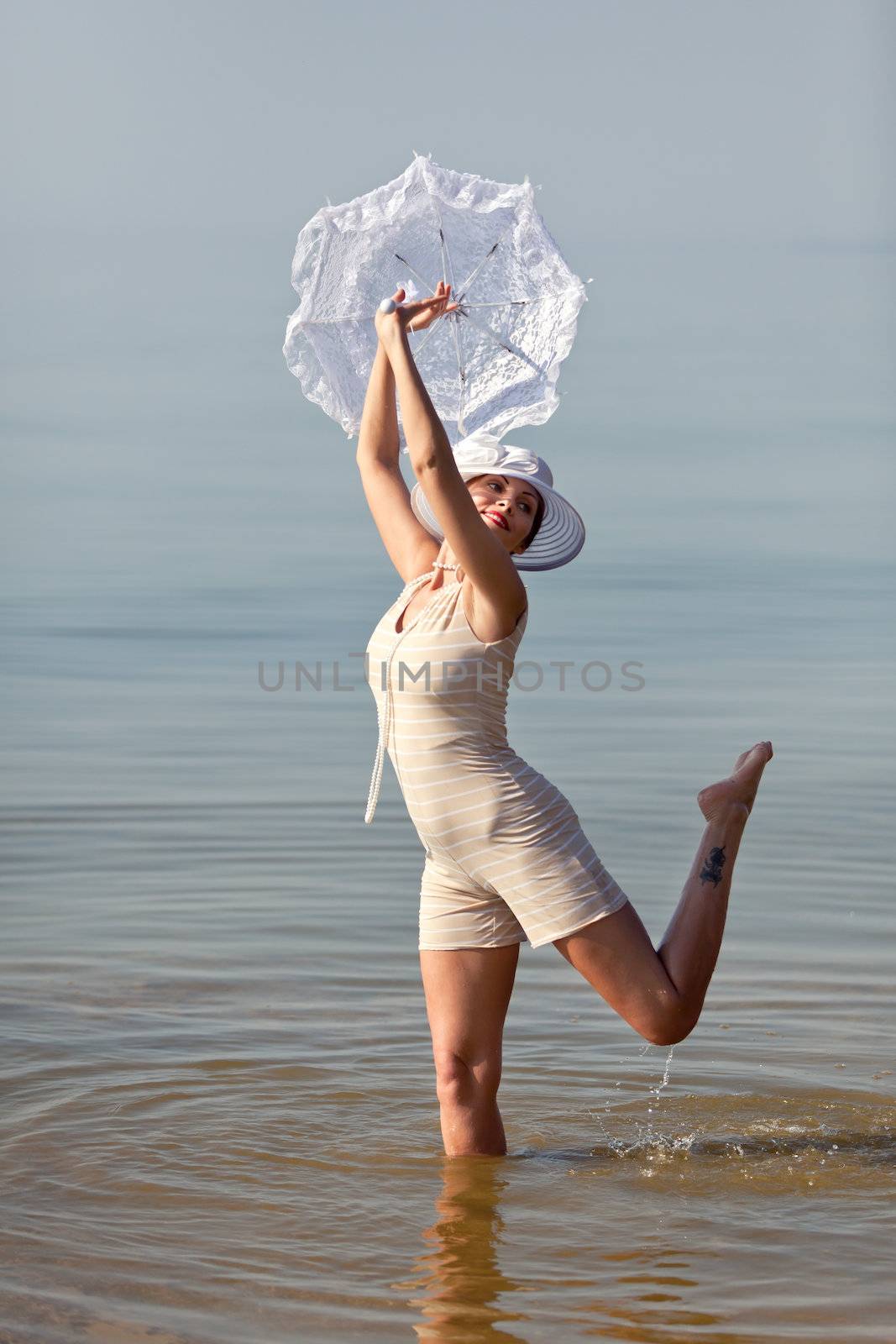 Woman in a striped retro bathing suit with a white parasol against the sea