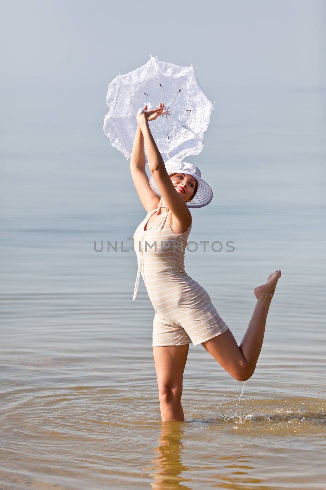 Woman in a striped retro bathing suit with a white parasol against the sea