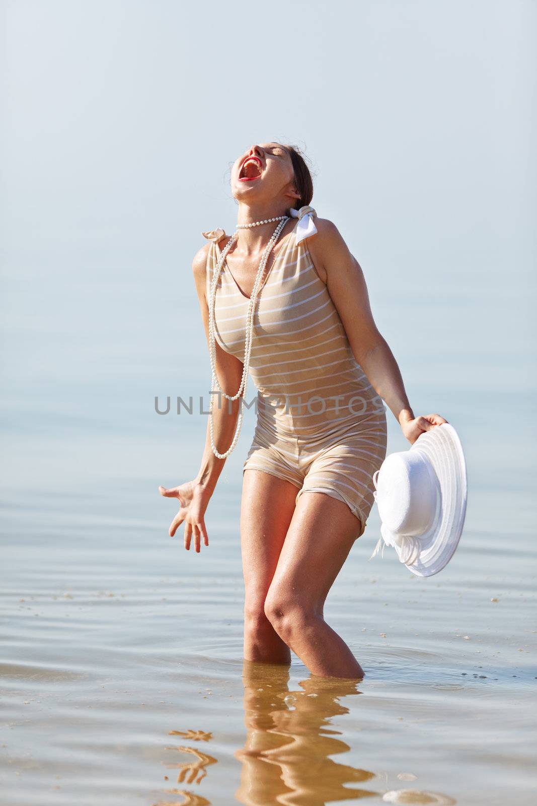 Woman in a striped retro bathing suit in the white hat cried against the sea