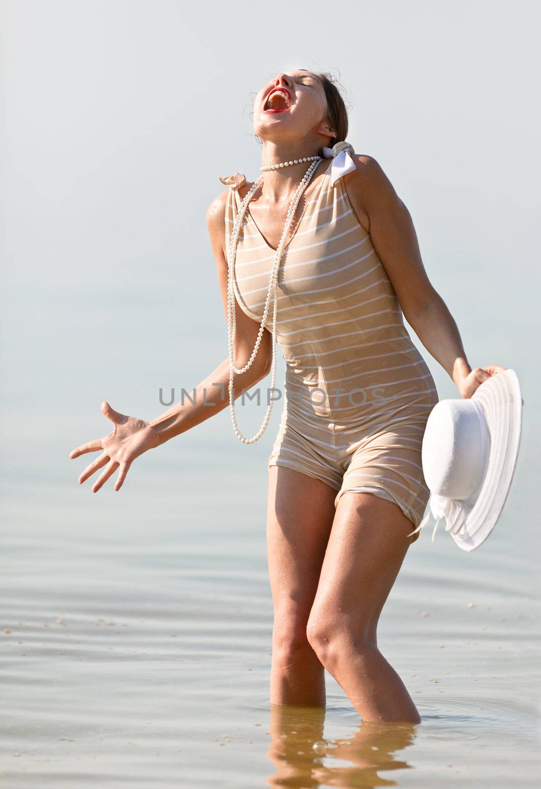 Woman in a striped retro bathing suit in the white hat cried against the sea