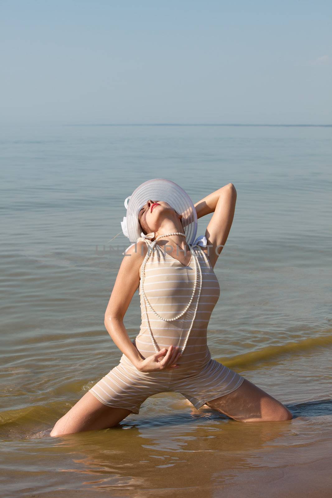 Woman in a striped retro bathing suit in the white hat posing against the sea