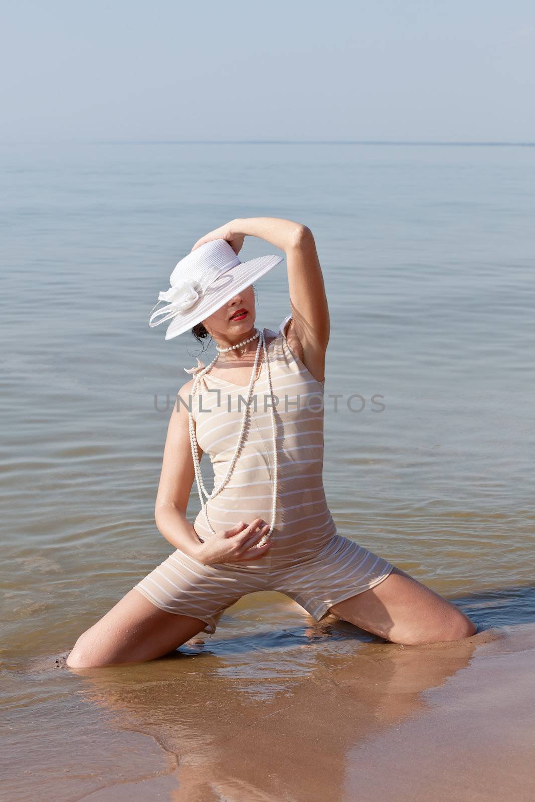 Woman in a striped retro bathing suit in the white hat posing against the sea