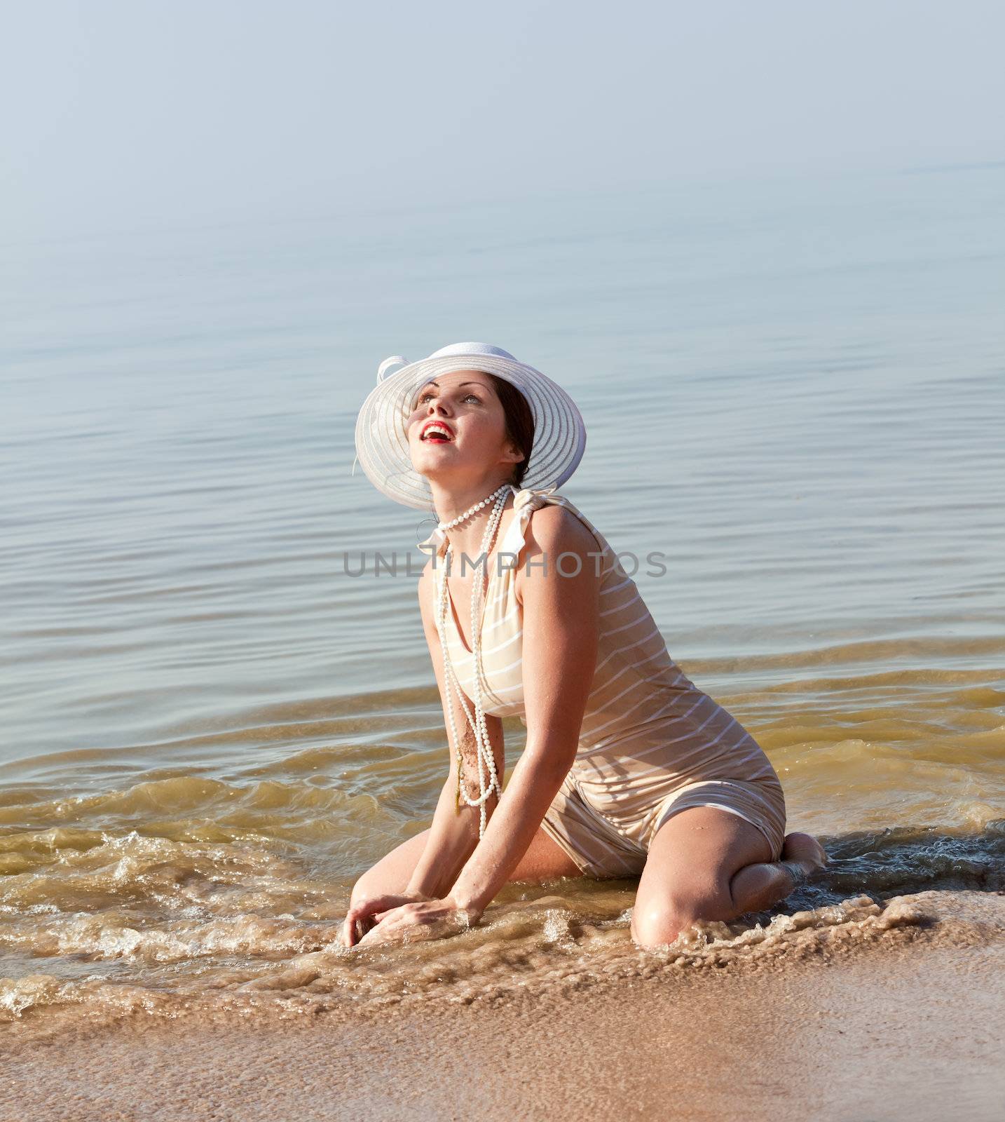 Woman in a striped retro bathing suit kneeling in the water at the beach