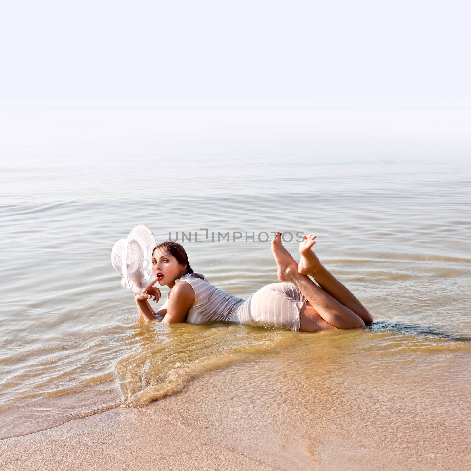 Woman in retro bathing suit and white hat lies in the water at the beach with room for text